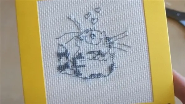 В руке держат открытку с вышитым серыми нитками котом